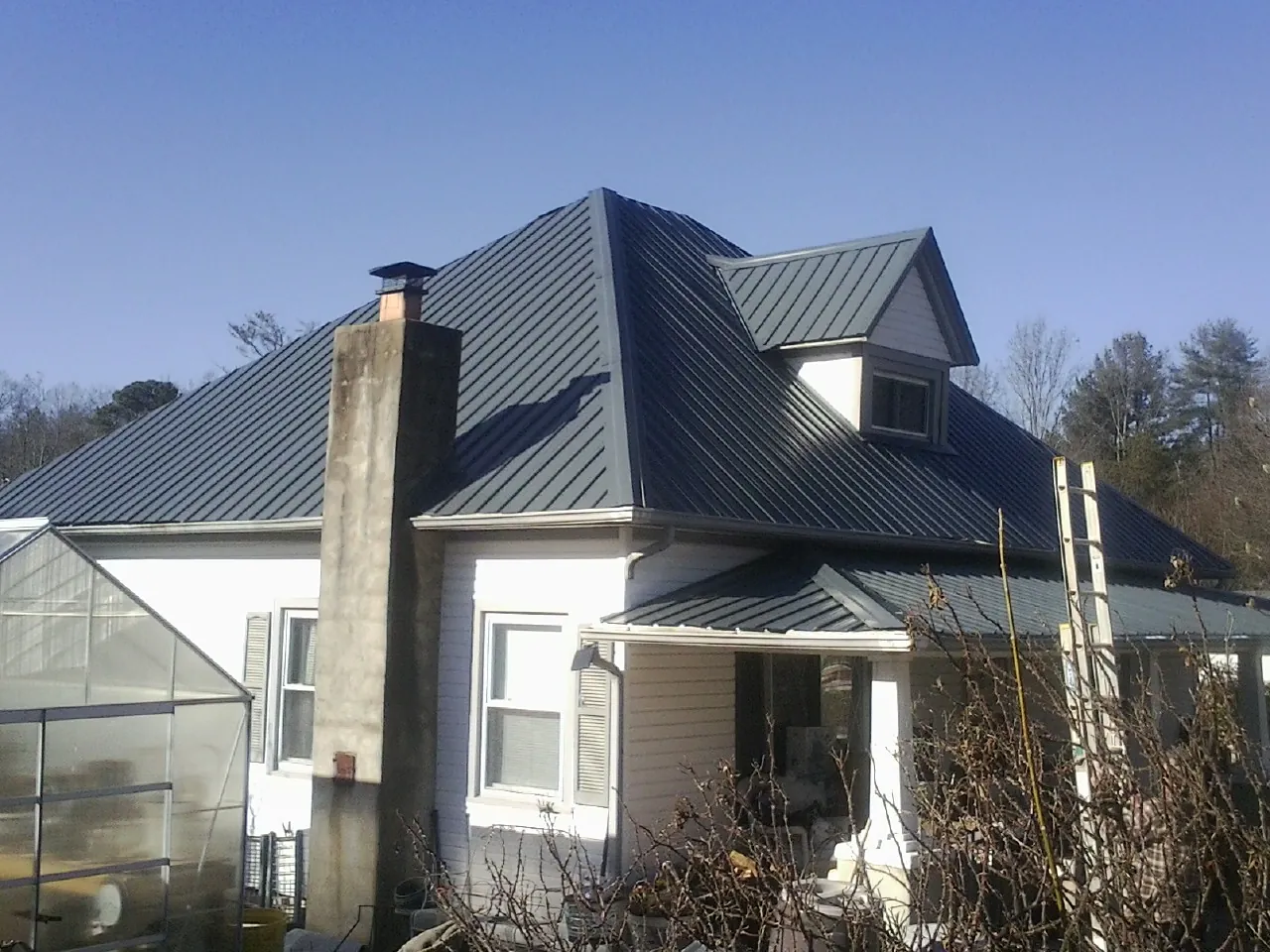 Dark blue standing seam metal roof on a white farmhouse with dormer — Slate & Tile Roof Repair by Roofing Brothers in Snyder